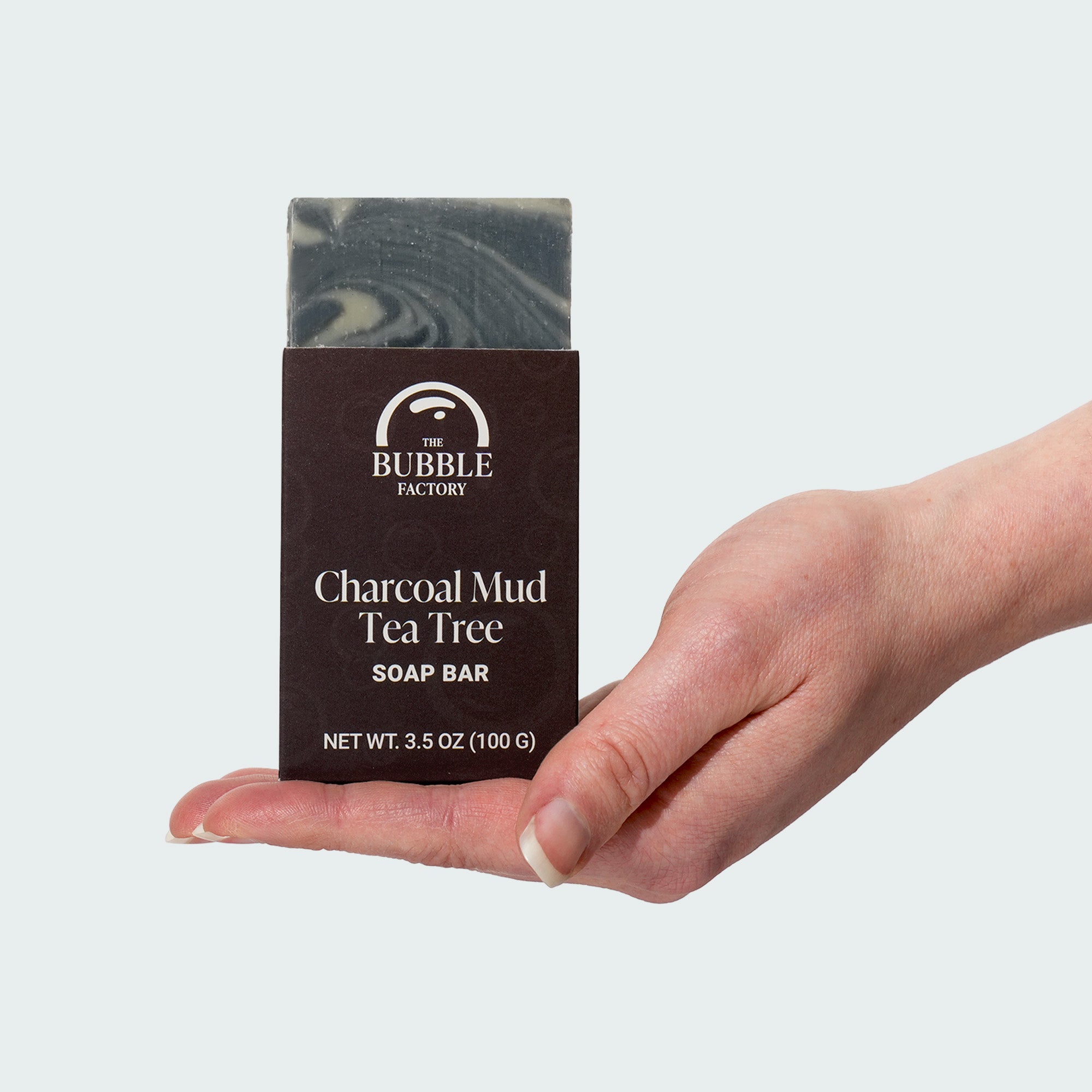 Hand holding a bar of charcoal mud tea tree soap